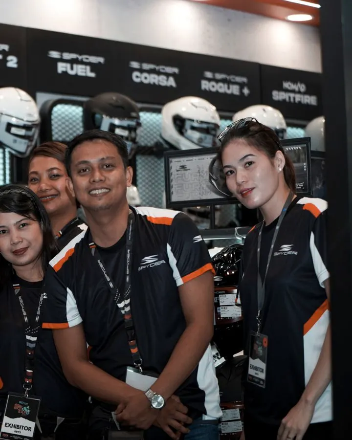 Booth staff in front of the Spyder helmet wall at a moto expo